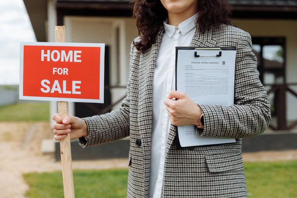 Woman holding "Home for Sale" sign and clipboard