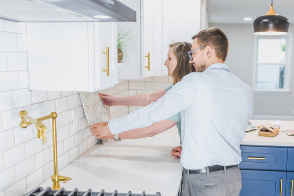 Man and woman holding up tile to kitchen backsplash